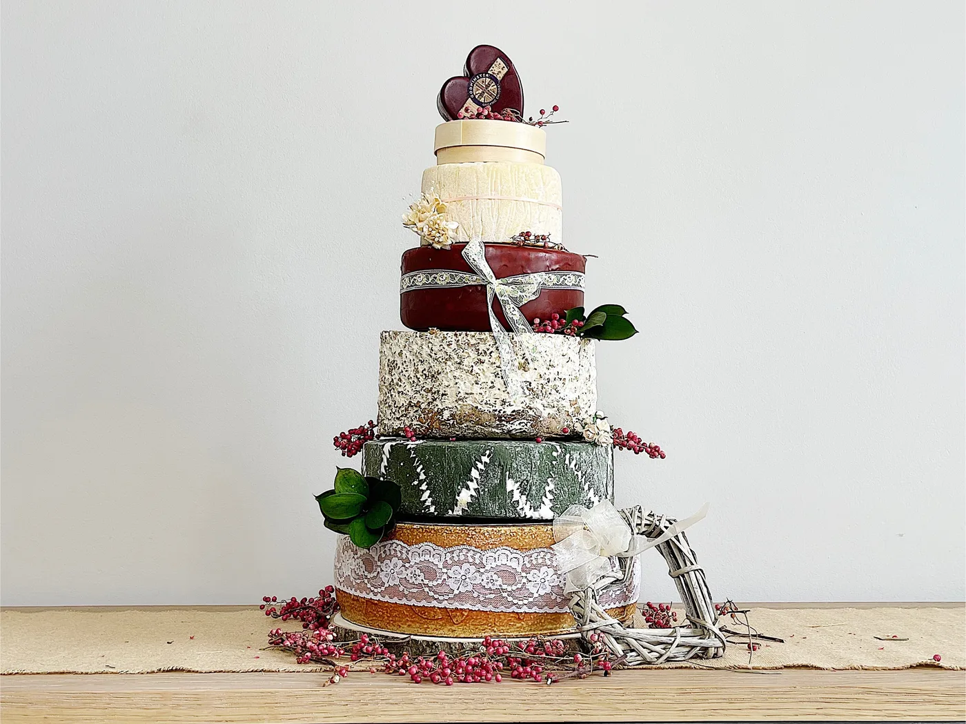 A tall tiered cheese wedding cake built from stacked whole cheese wheels, garnished with dried flowers and berries