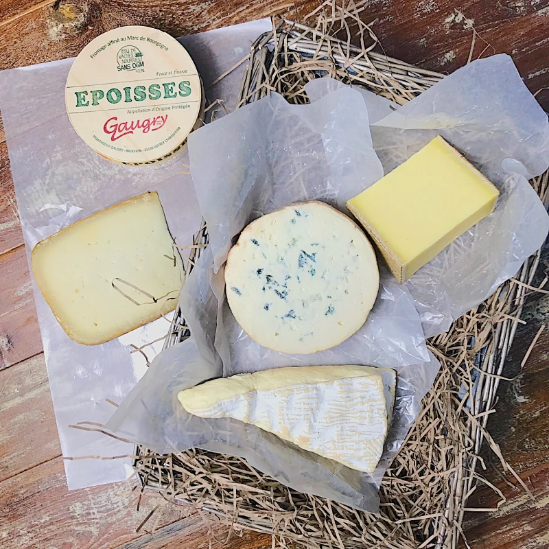 A Guide to French Cheese: The Classics and What to Drink with Them 24 French cheese selection with Epoisses, Comte, blue and Brie wrapped in paper on straw