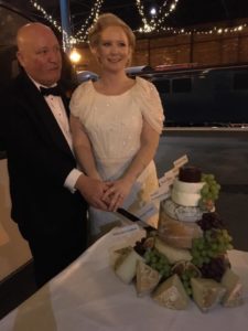 a couple stand next to their cheese cake tower